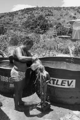 O menino Guilherme toma banho com água trazida por caminhões-pipa, que enchem as caixas d'água das casas na comunidade. Integrantes da aldeia relatam um forte cheiro de cloro na água enviada pela Samarco ¬– o uso desta provocou alergias e irritações na pele de muitas crianças. Alguns pais optam por banhar seus filhos com água mineral engarrafada