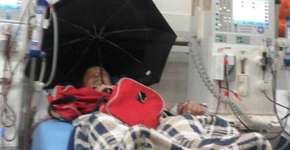 Idoso se protege de goteira com guarda-chuva em hospital