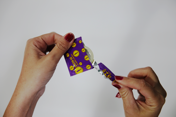 Abra o preservativo rasgando apenas a embalagem pelos vincos das bordas